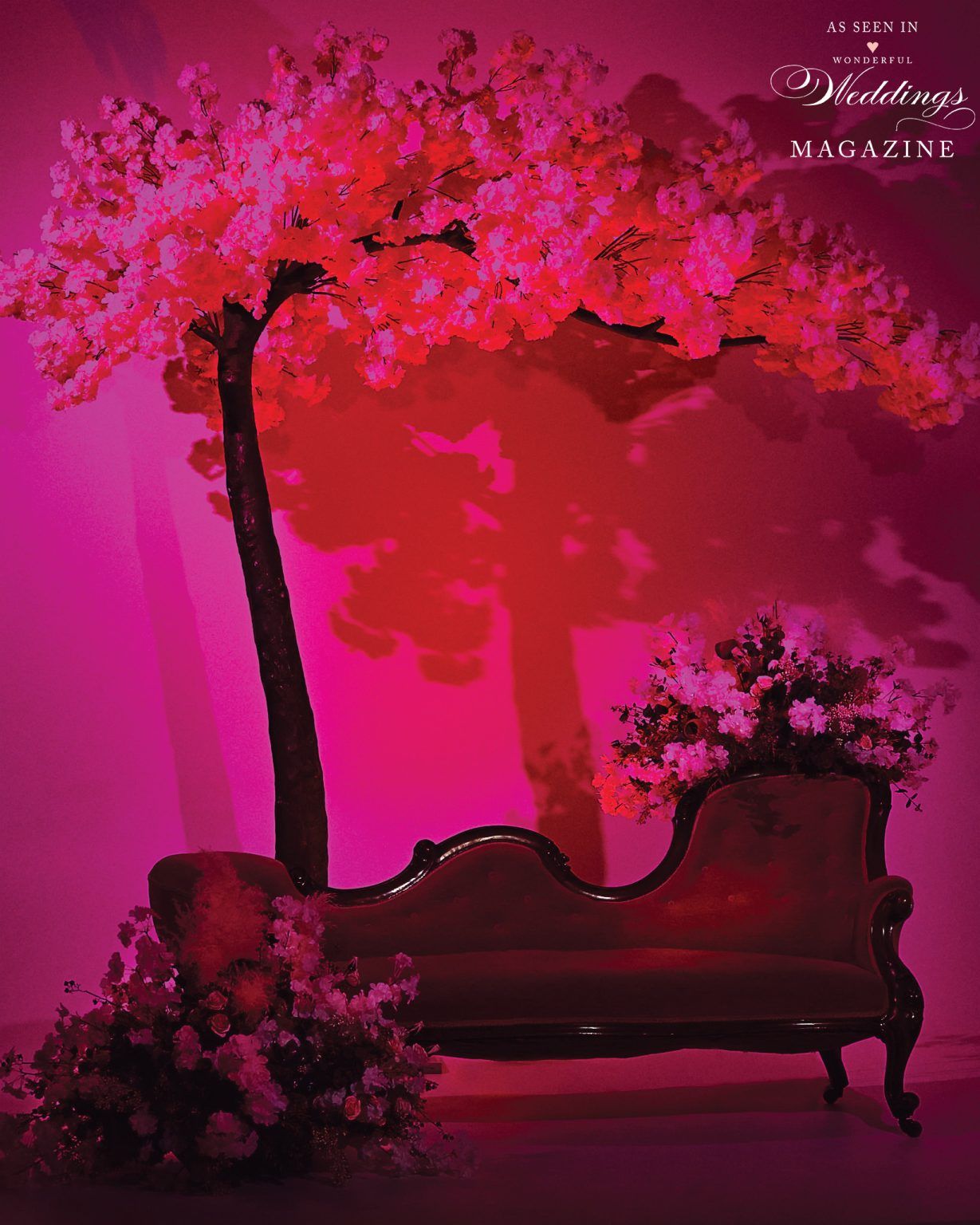 A couch is sitting under a tree with pink flowers.