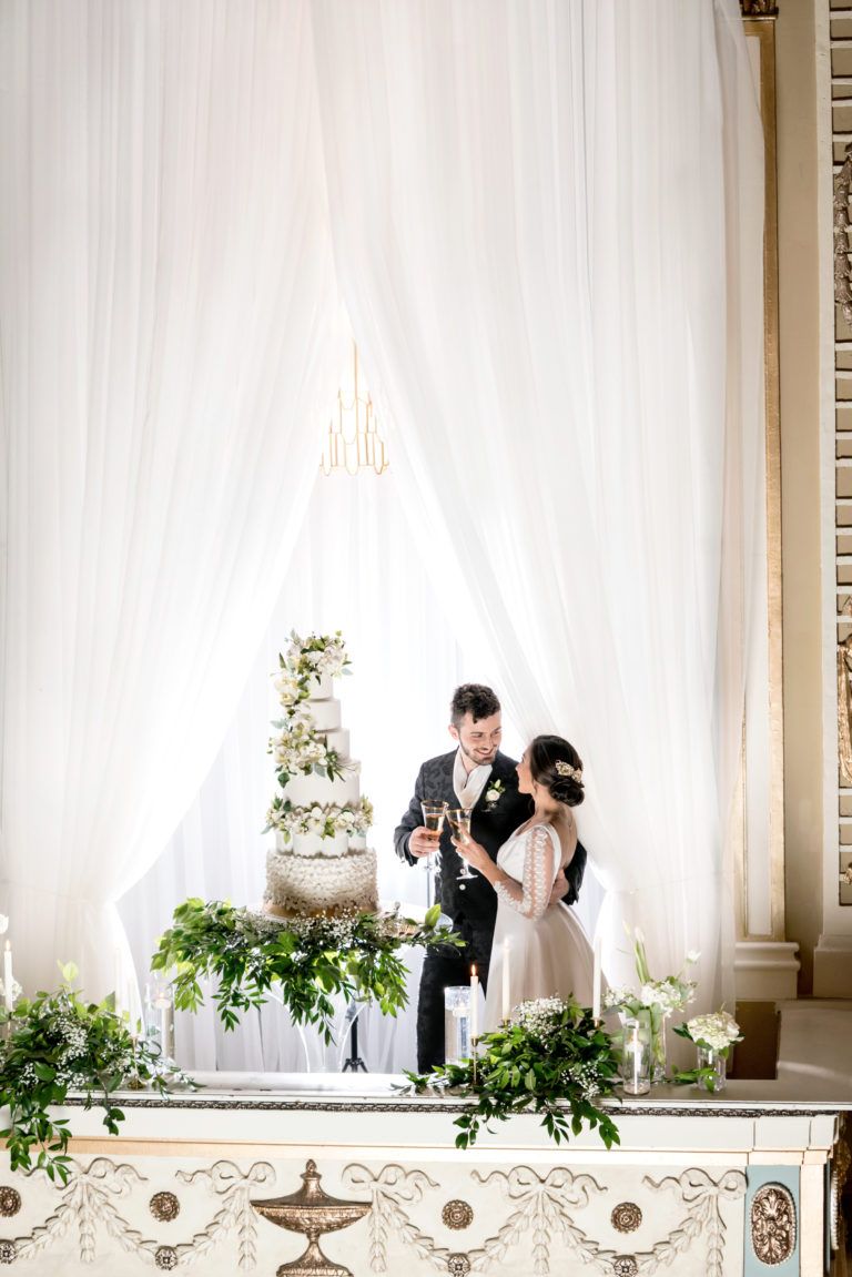 A bride and groom are standing in front of a wedding cake.