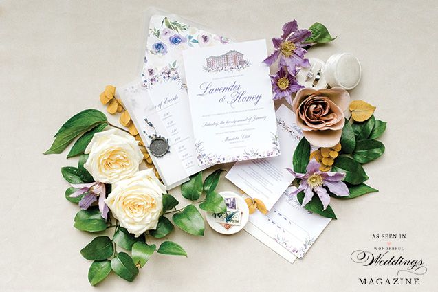A wedding invitation is surrounded by flowers and leaves on a table.