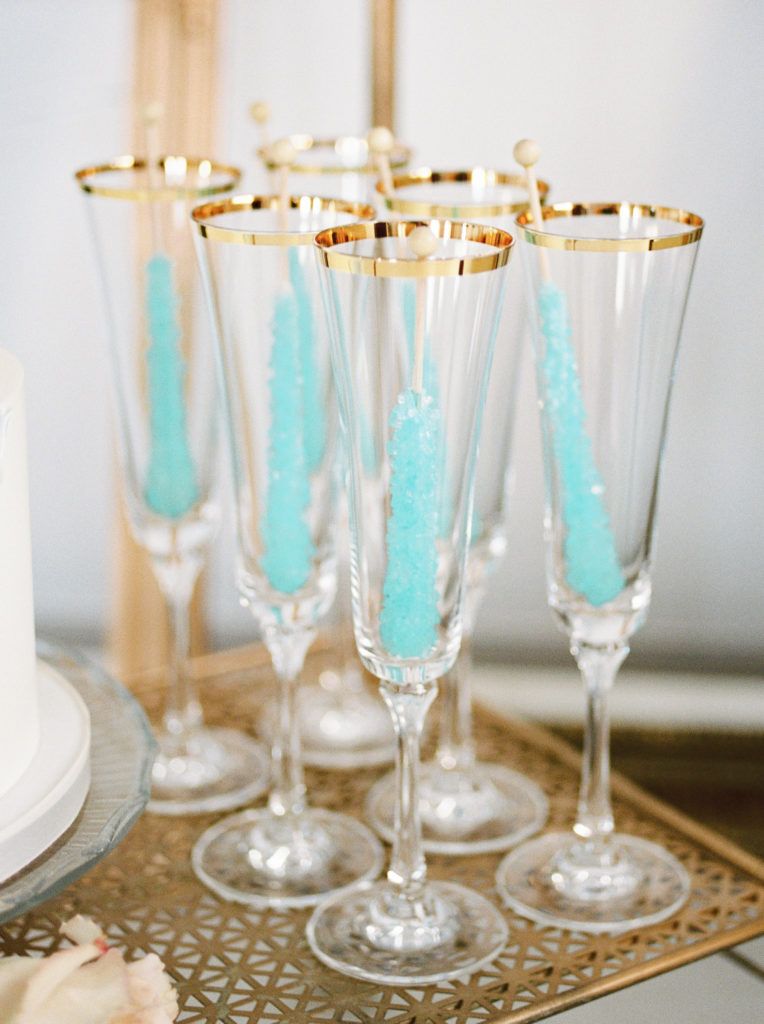 A tray of champagne flutes with blue sugar cubes in them.