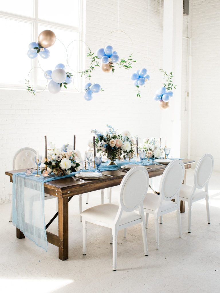A long wooden table with white chairs and balloons hanging from the ceiling.