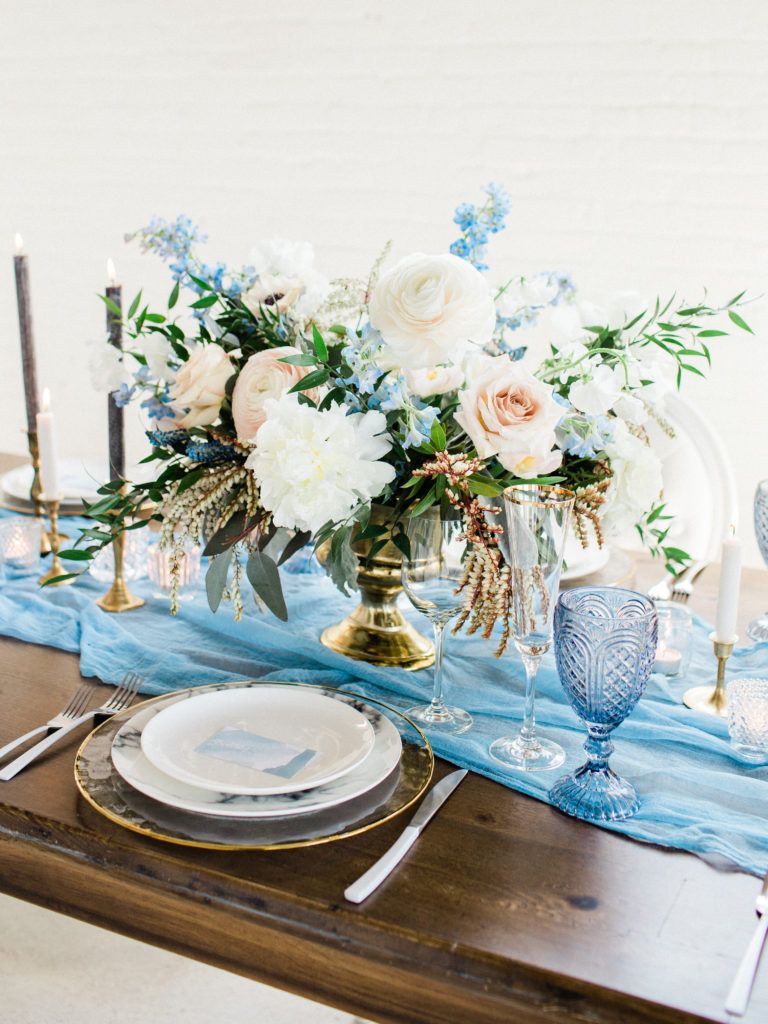 A wooden table with plates , glasses , candles and a vase of flowers on it.