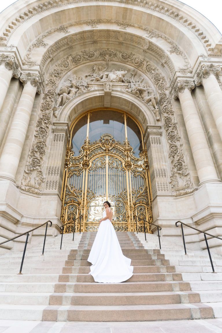 A bride in a white dress is standing on a set of stairs in front of a building.