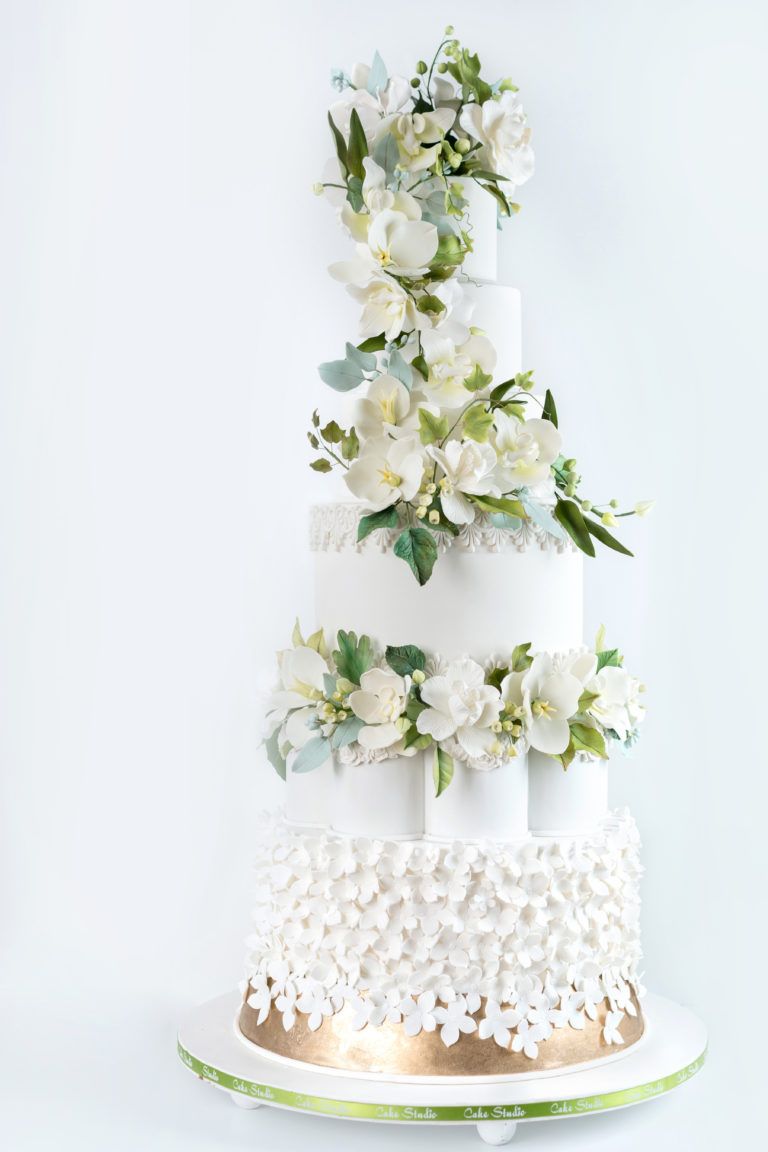 A white wedding cake with white flowers and green leaves on a white background.