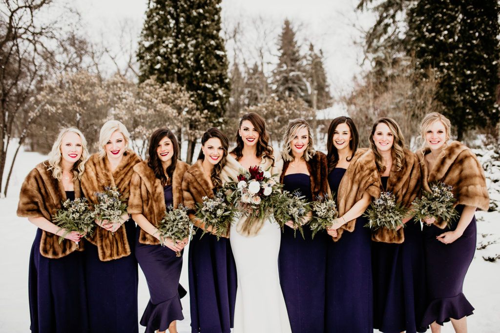 A bride and her bridesmaids are posing for a picture in the snow.
