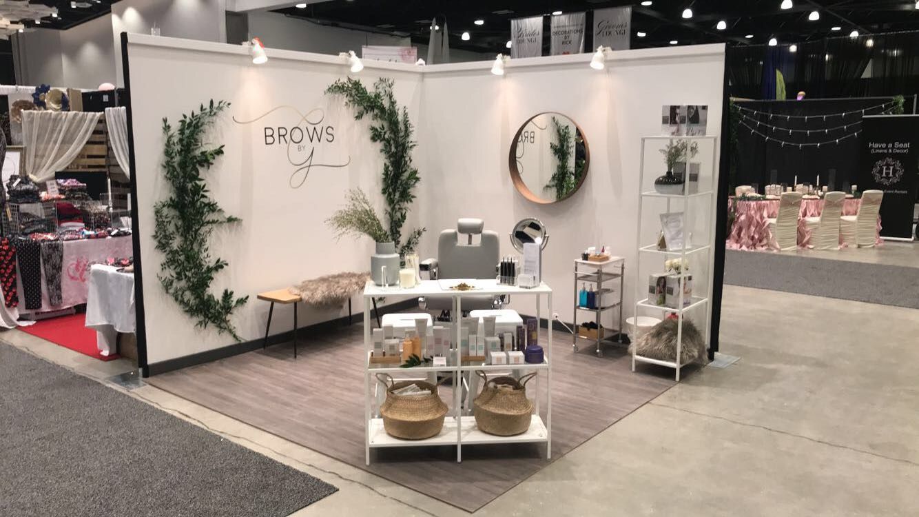 A booth at a convention with a white wall and shelves.