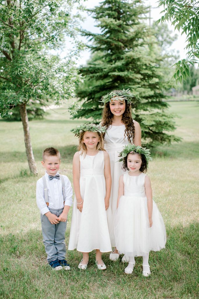 A group of flower girls and a ring bearer are posing for a picture in front of a pine tree.