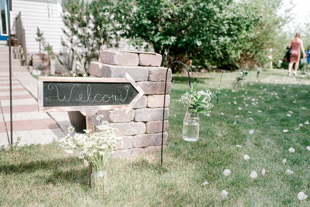 A chalkboard sign is sitting in the grass next to a brick wall.