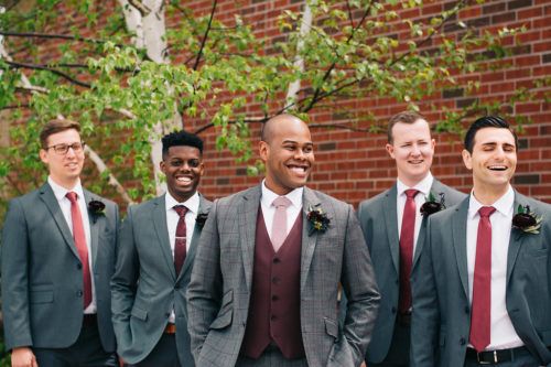 A groom and his groomsmen are posing for a picture in front of a brick wall.