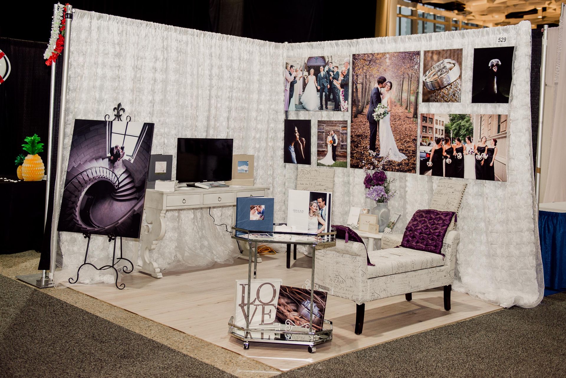 A booth with a chair , table , computer , and pictures on the wall.