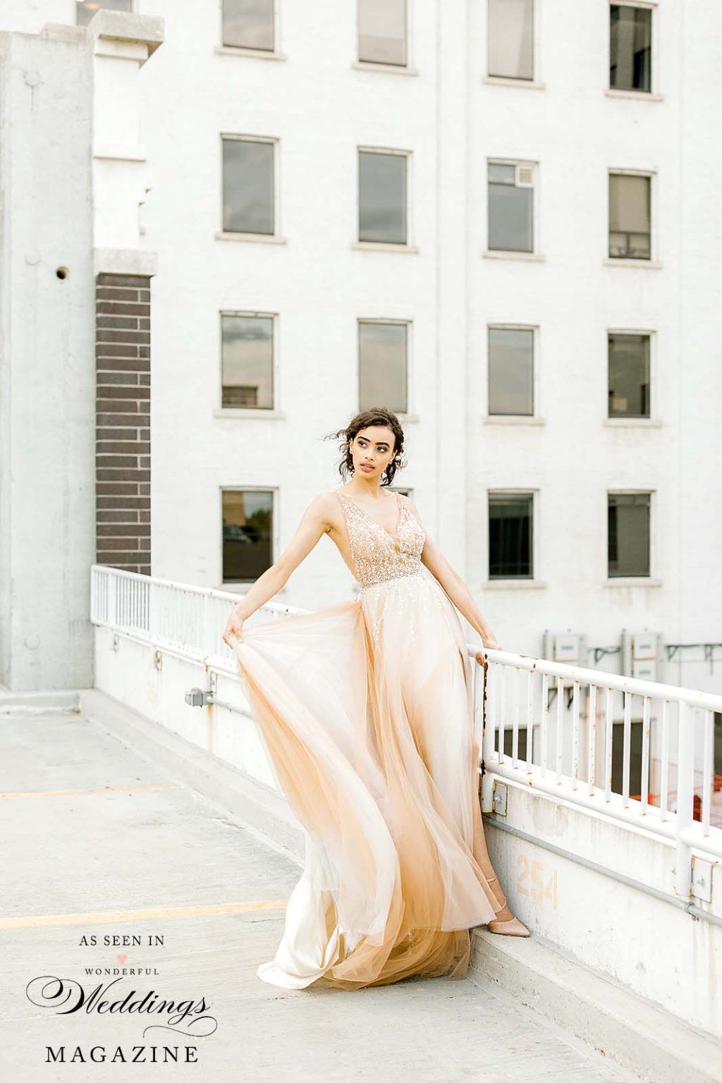 A woman in a long dress is standing on a balcony next to a building.