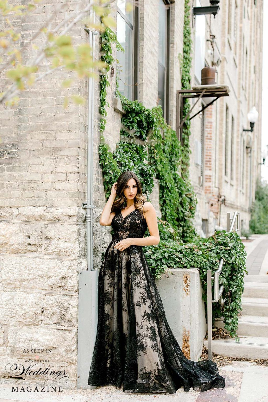 A woman in a black lace dress is standing in front of a building.