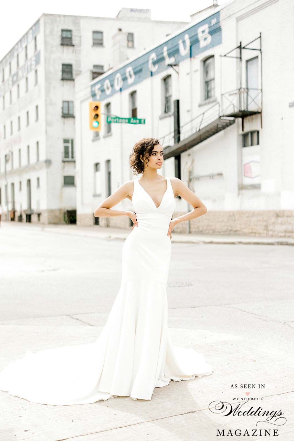 A woman in a white dress is standing in front of a building.