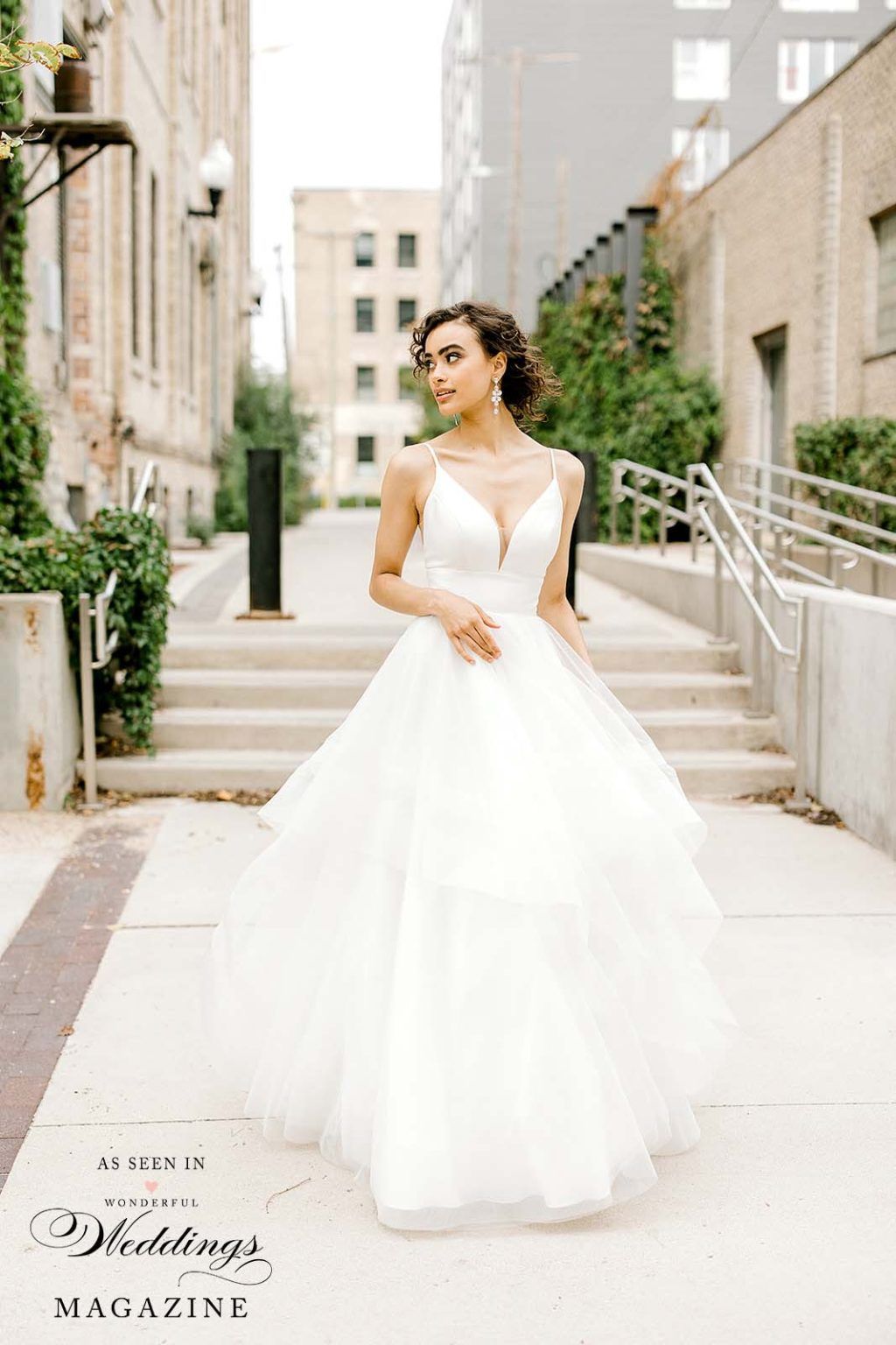 A bride in a wedding dress is standing on a sidewalk in front of a building.
