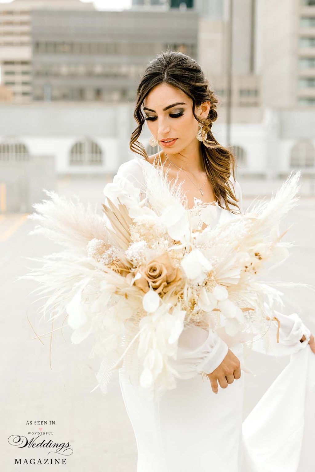 A bride in a white dress is holding a bouquet of dried flowers.