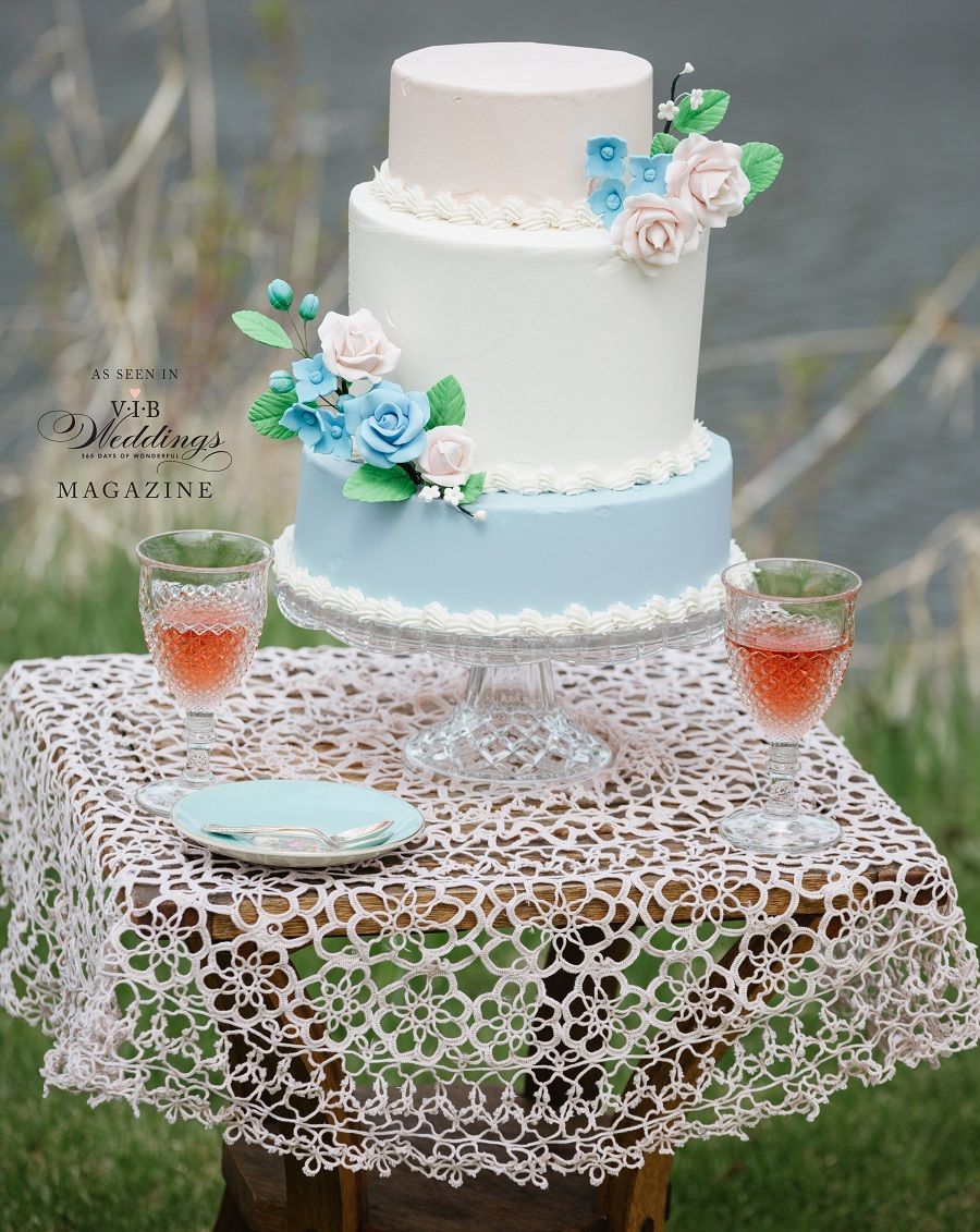 A white and blue wedding cake is sitting on a table with glasses of wine.