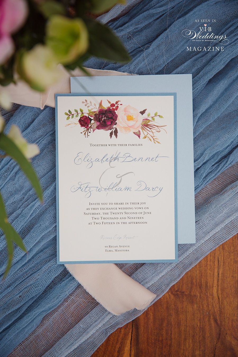 A wedding invitation is sitting on a wooden table next to a bouquet of flowers.