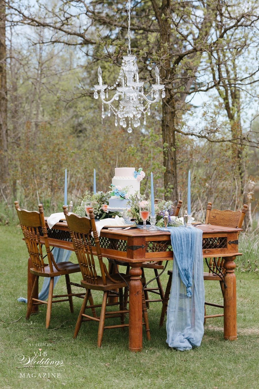 A wooden table and chairs in a field with a chandelier hanging from the ceiling.