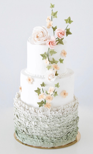 A three tiered wedding cake with roses and leaves on top.