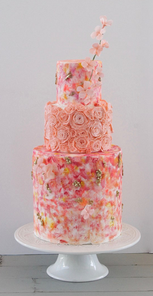 A pink wedding cake is sitting on top of a white cake stand.