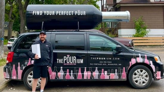 A man is standing in front of a minivan that says the pourium on it.