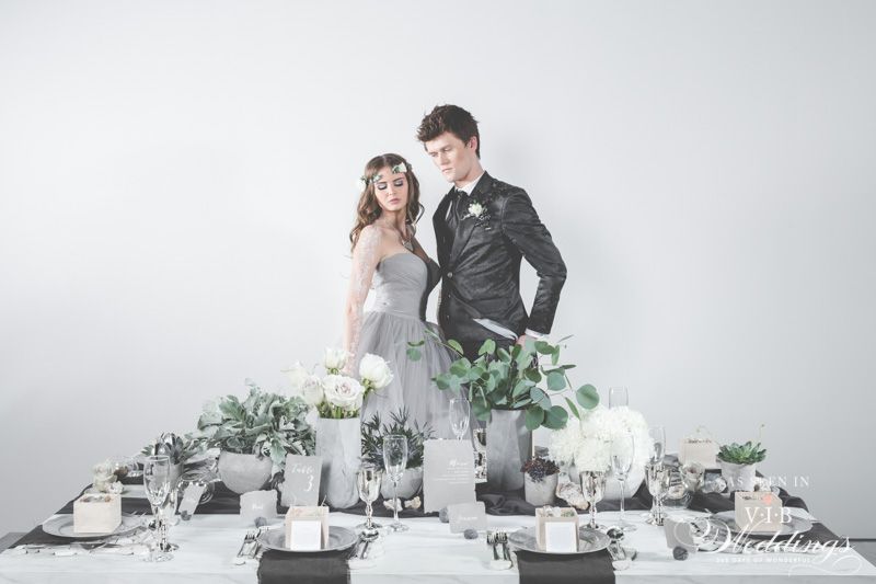 A bride and groom are standing next to a table set for a wedding reception.