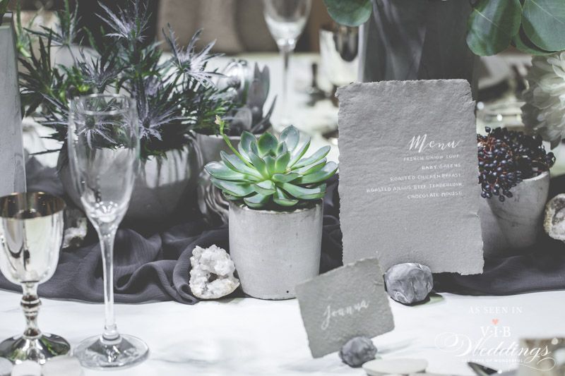 A table set for a wedding reception with a menu , wine glasses , and succulents.