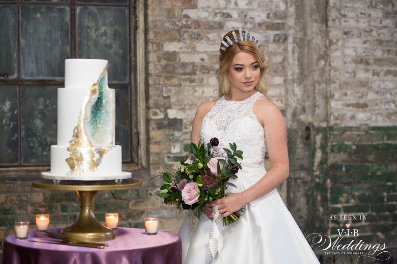 A bride in a wedding dress is standing in front of a wedding cake.