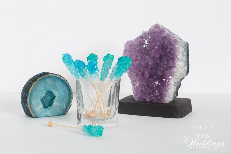 A glass filled with blue rock candy next to a purple crystal.