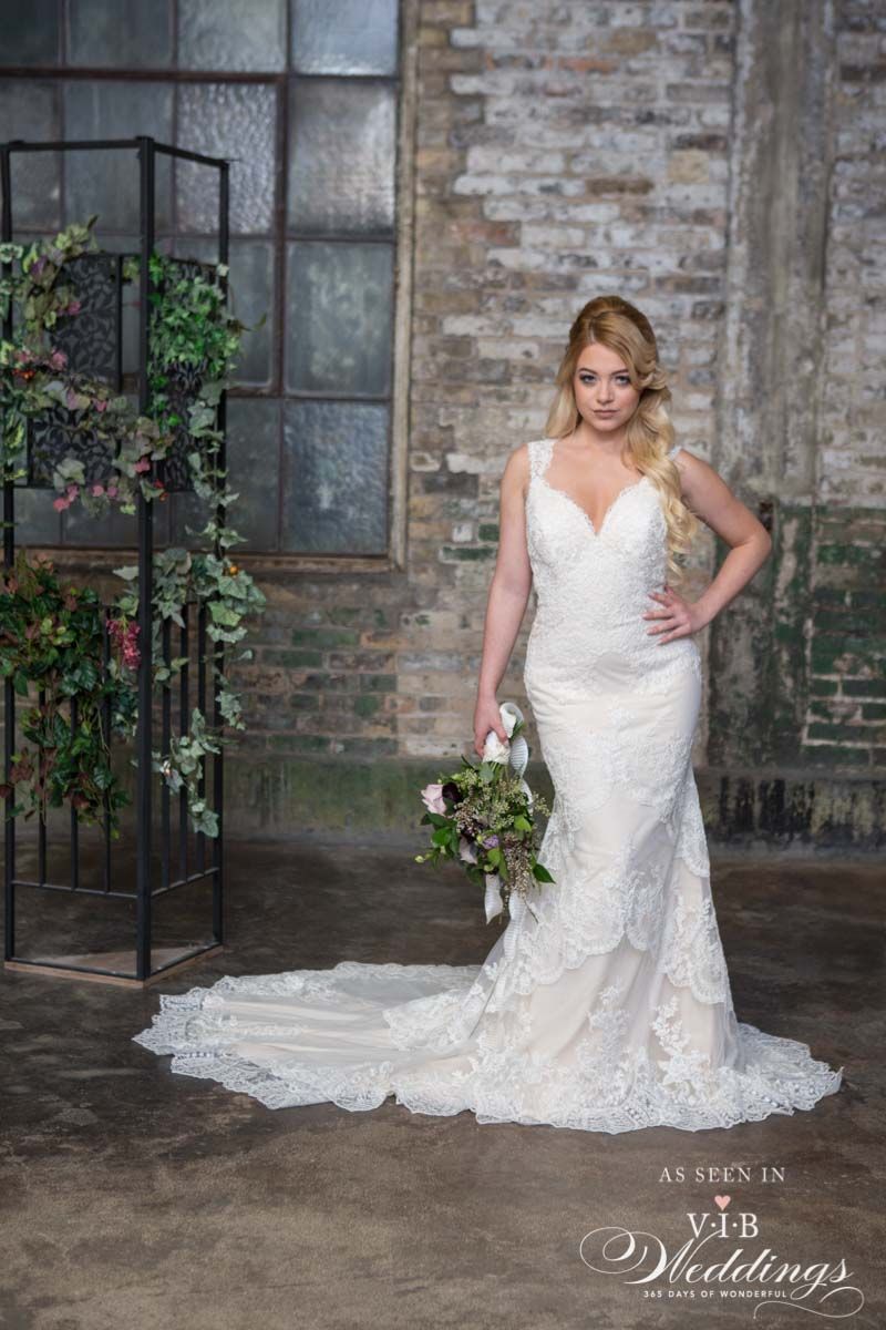 A woman in a wedding dress is standing in front of a brick wall holding a bouquet of flowers.