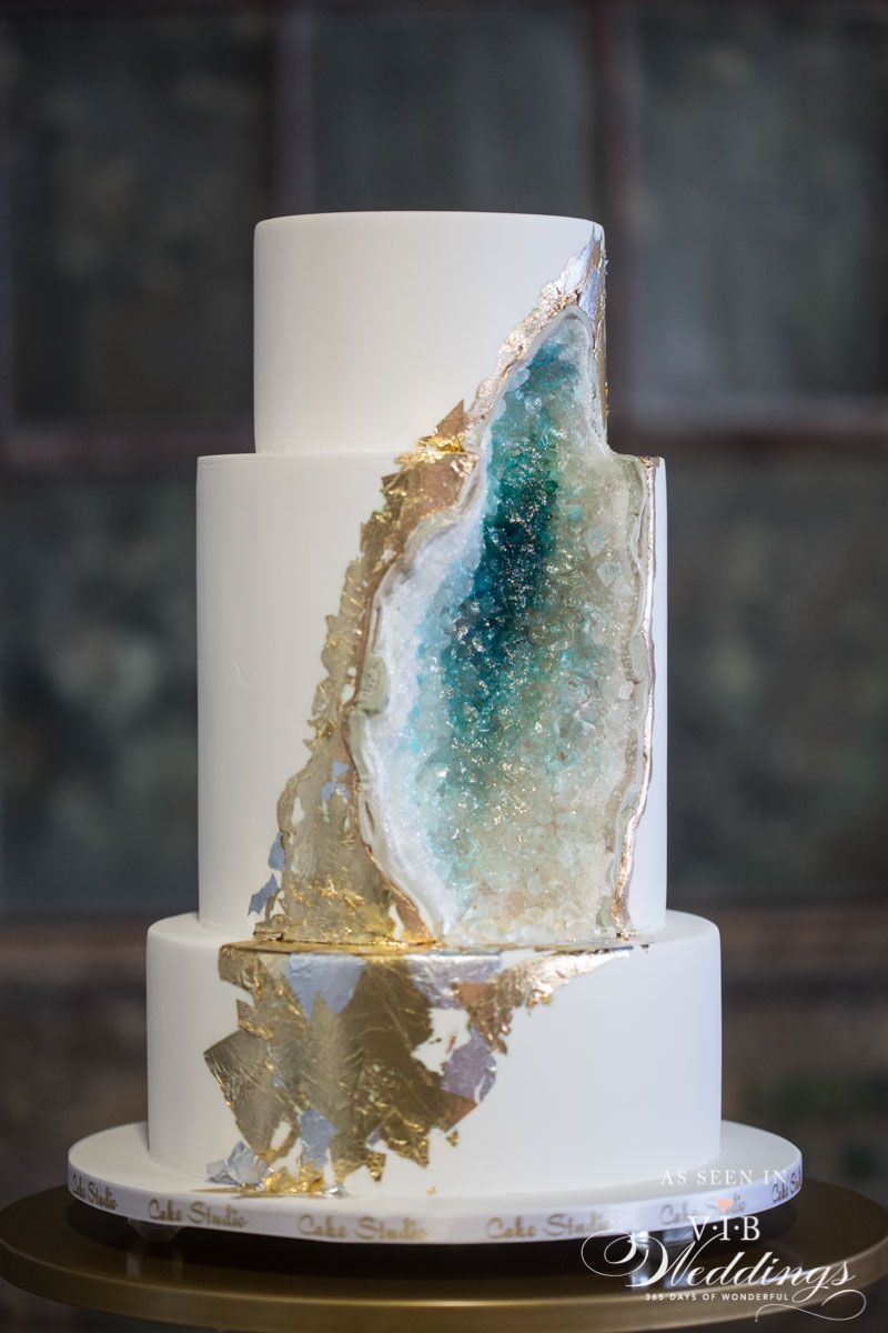A white wedding cake with a blue and gold slice on top of it.