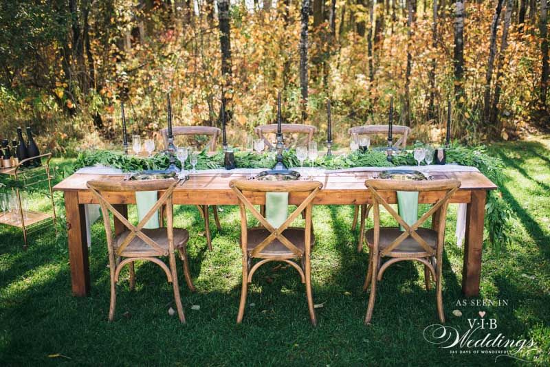 A long wooden table with chairs in front of a forest.