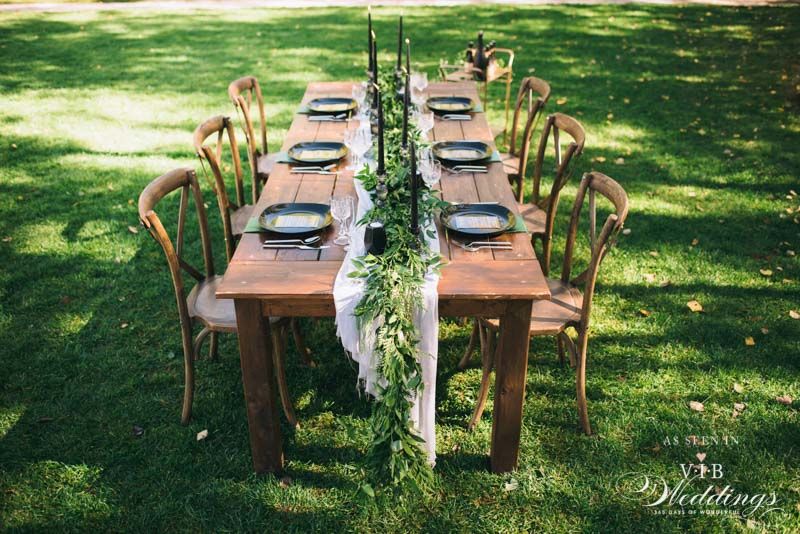 A long wooden table and chairs are sitting on top of a lush green field.