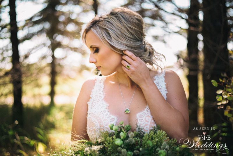 A woman in a wedding dress is standing in the woods holding a bouquet of flowers.