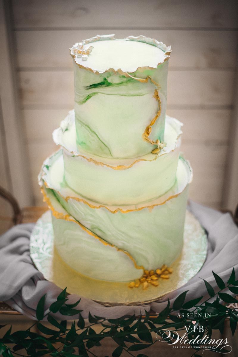 A green and gold wedding cake is sitting on top of a wooden table.