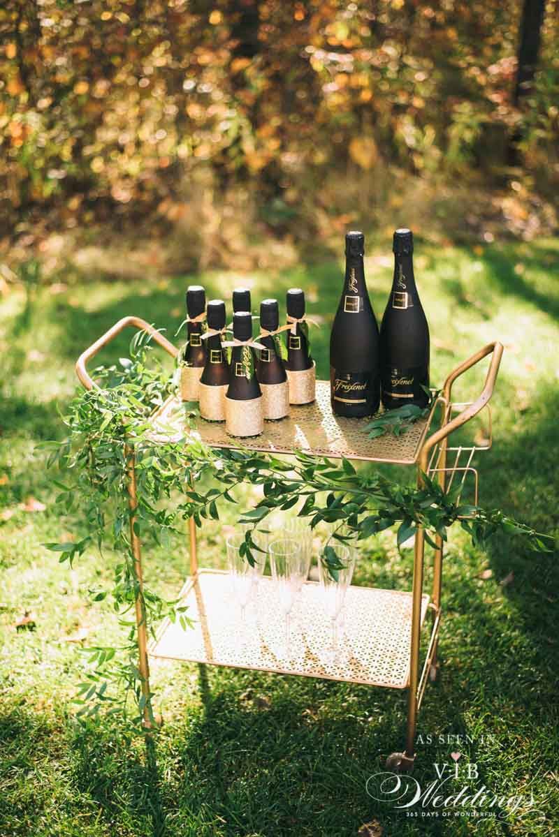 A bar cart filled with bottles of wine and glasses is sitting on top of a lush green field.