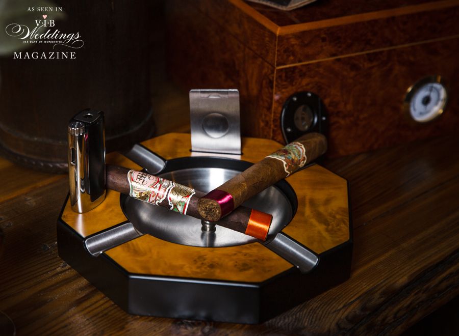 Two cigars are in an ashtray on a wooden table.