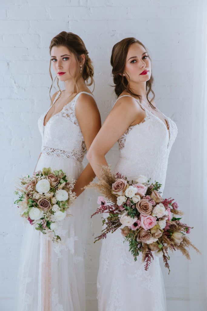 Two brides are standing next to each other holding bouquets of flowers.
