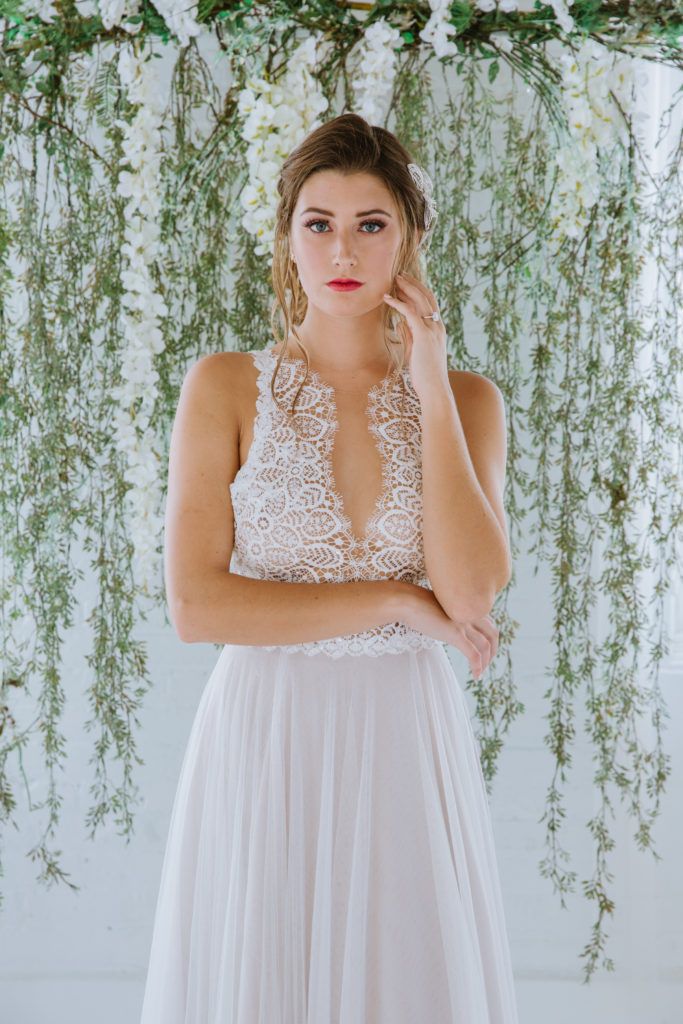 A woman in a wedding dress is standing in front of a wall of flowers.