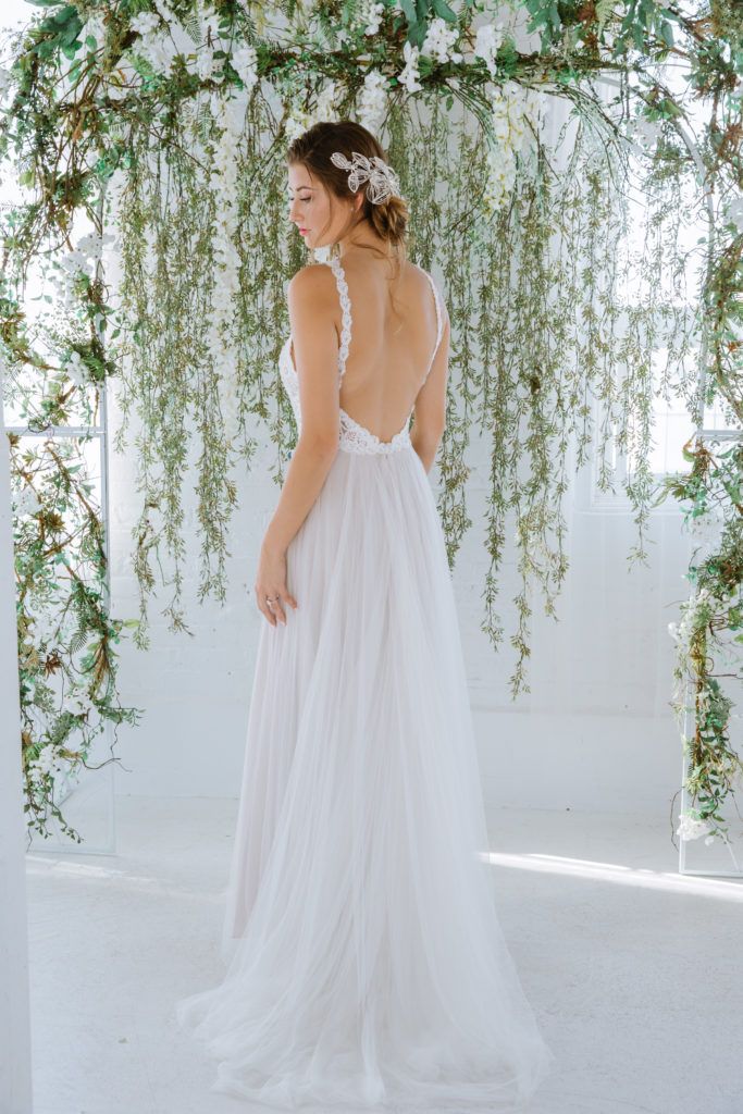 A woman in a white wedding dress is standing in front of a floral arch.
