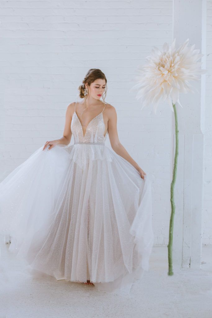 A woman in a wedding dress is standing next to a large flower.