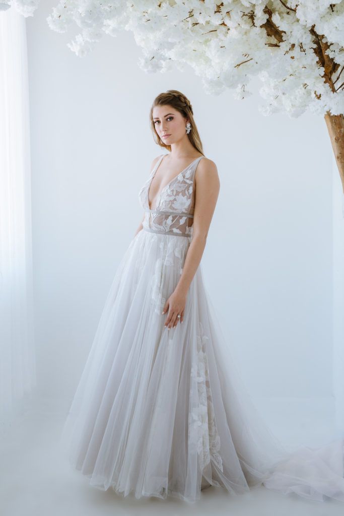 A woman in a wedding dress is standing in front of a tree with white flowers.