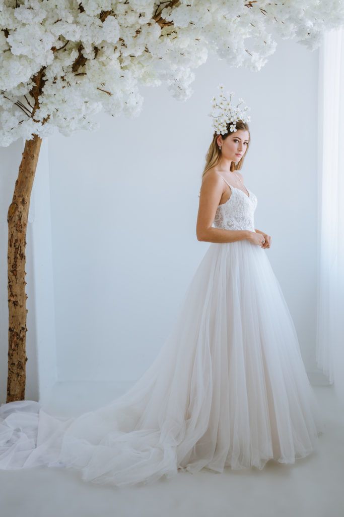 A woman in a wedding dress is standing in front of a tree with white flowers.