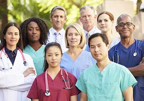 Group of healthcare professionals in colorful scrubs and lab coats standing outdoors