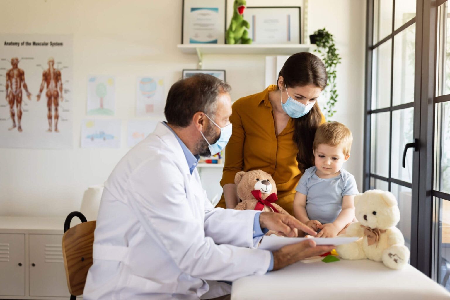 Doctor examining a child with teddy bears in a bright clinic room