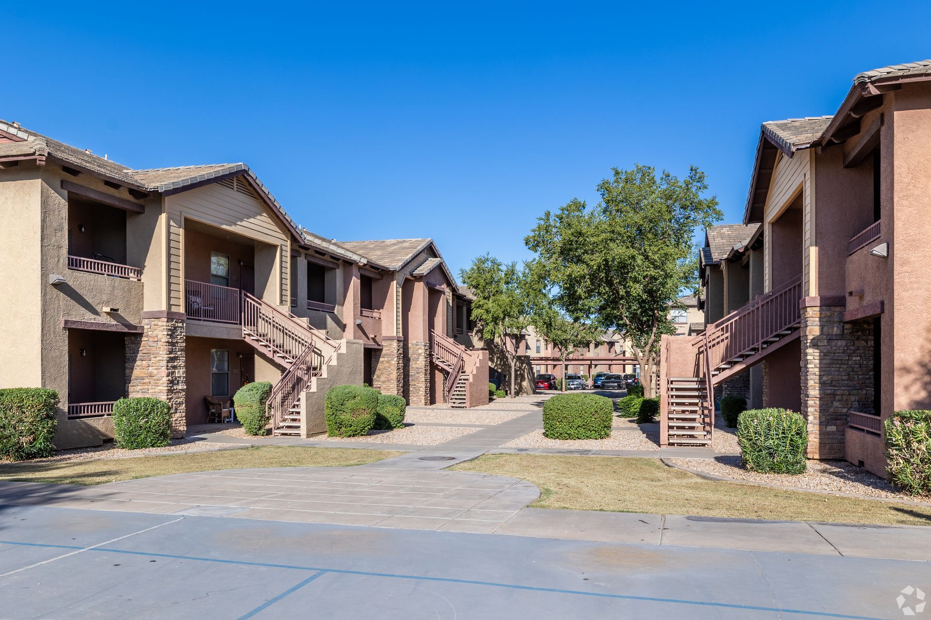 Two-story apartment buildings with stucco walls and stone accents face each other across a paved courtyard.