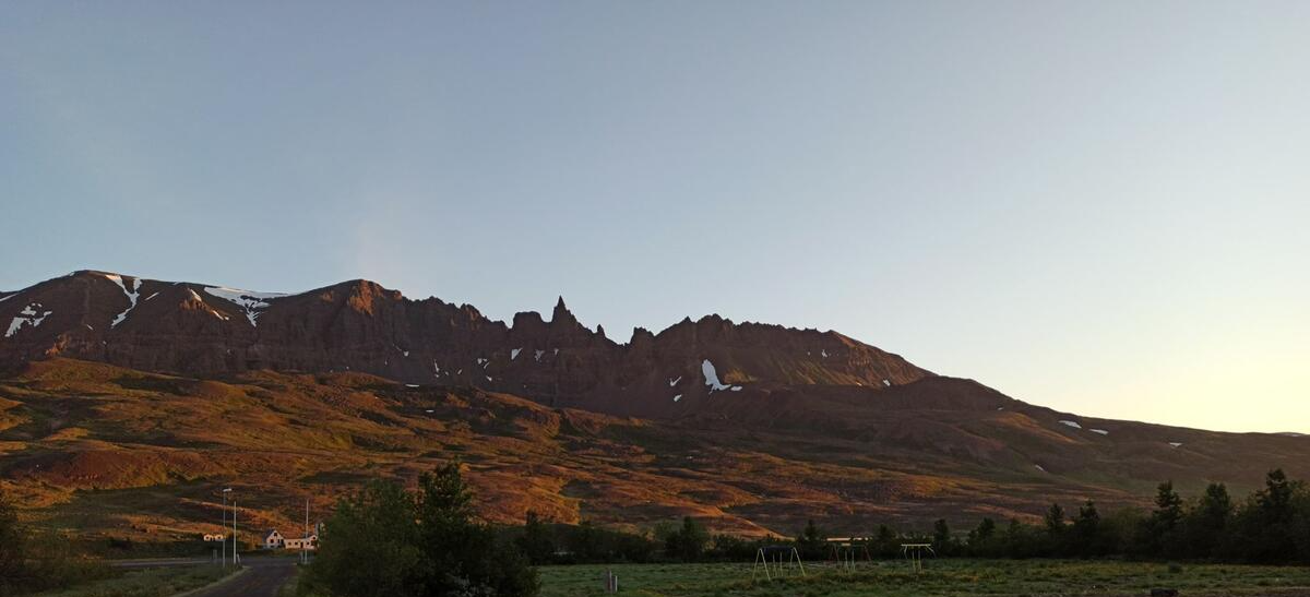 Sunlit rocky mountain ridge above a green valley at dusk