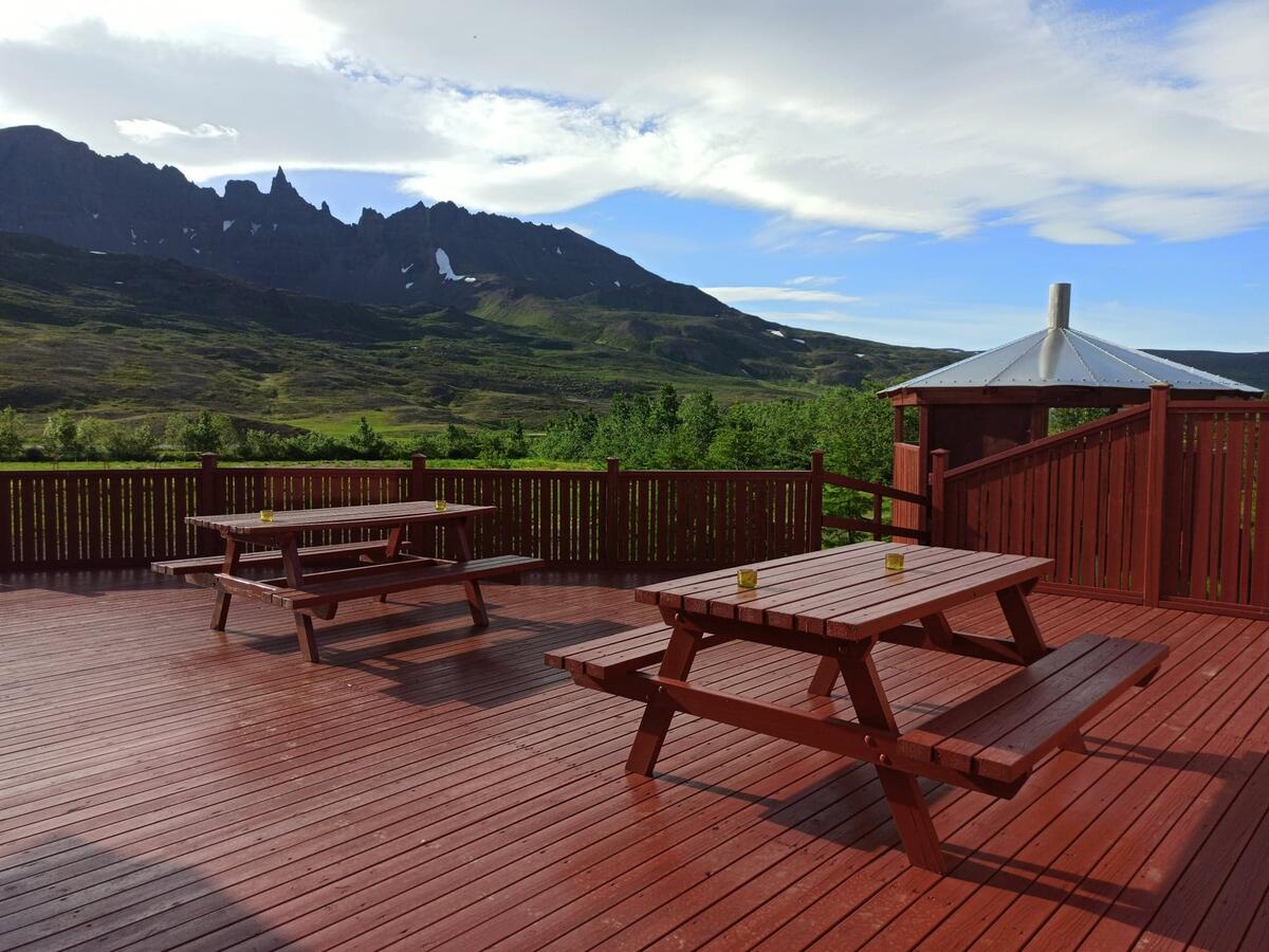 Red wooden deck with picnic tables overlooking green mountains under a partly cloudy sky
