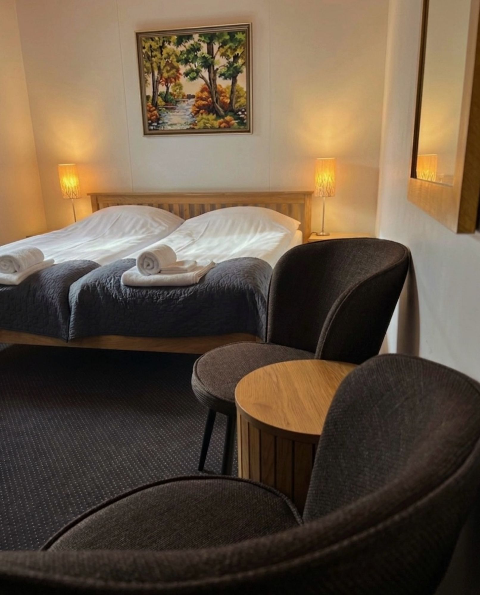 Cozy hotel room with two twin beds, bedside lamps, and two chairs beside a small round table.