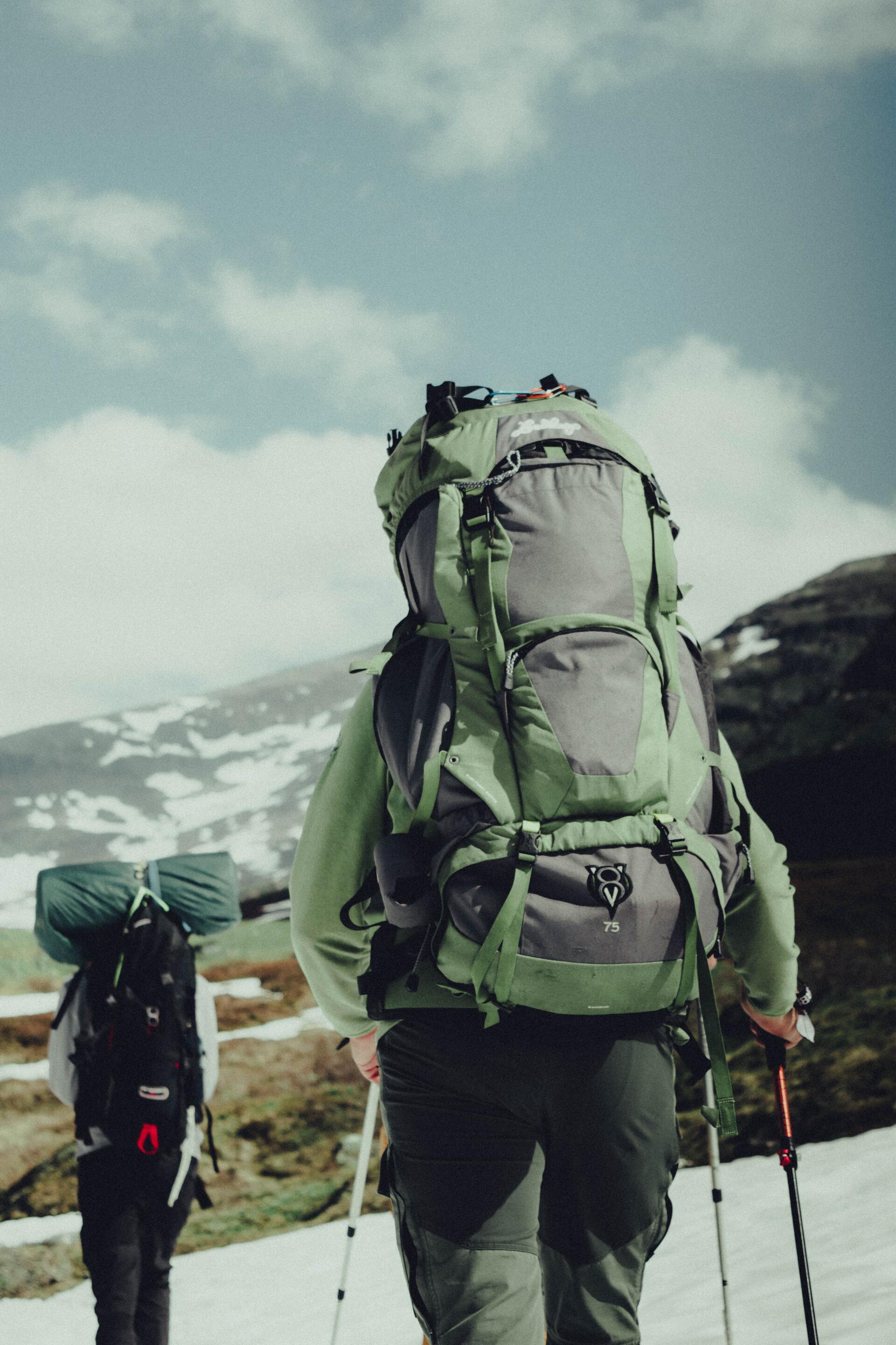 A person with a green backpack is walking in the snow
